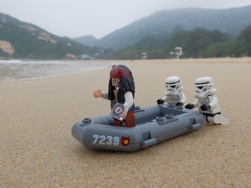 This is a close look at lego Jack Sparrow, lego storm troopers and a lego lifeboat on a beach.