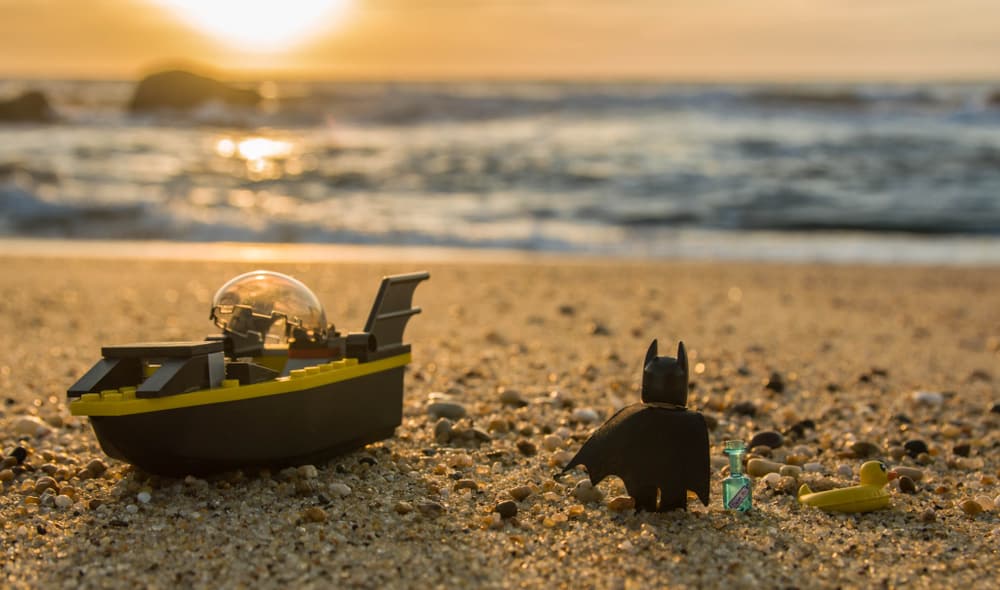 A close look at at a lego batman with his lego batboat on a beach.