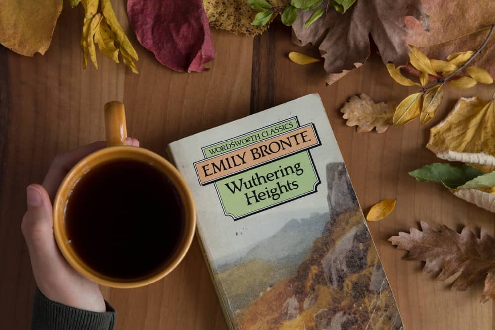 A woman drinking tea with her copy of Wuthering Heights.