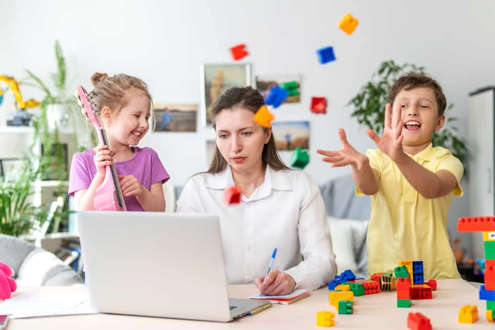 A woman trying to work at home while her two kids are playing beside her.