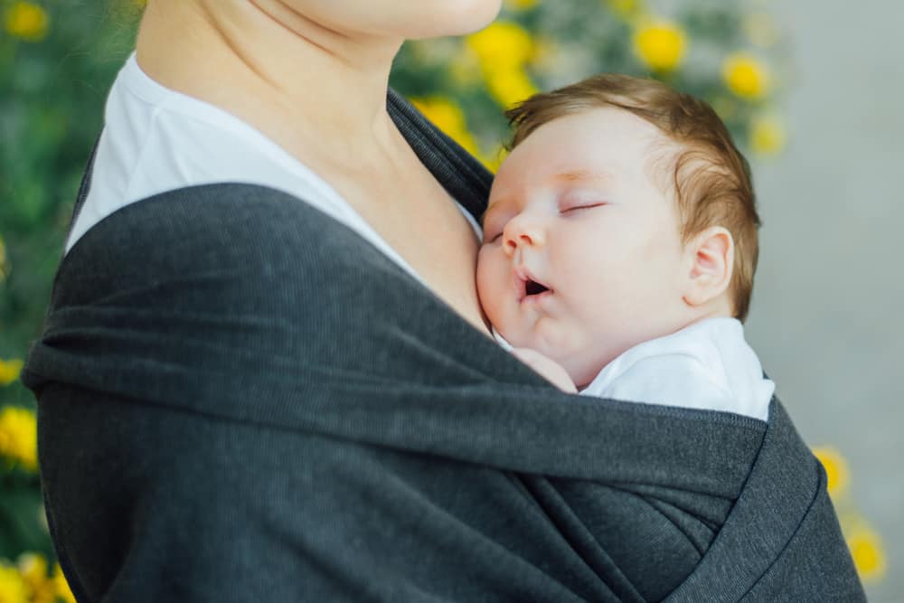 A close look at a baby sleeping in a wrap being carried by the mother.