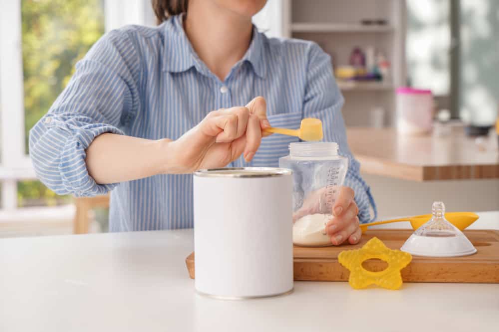 This is a close look at a woman preparing a bottle of milk with powdered formula.
