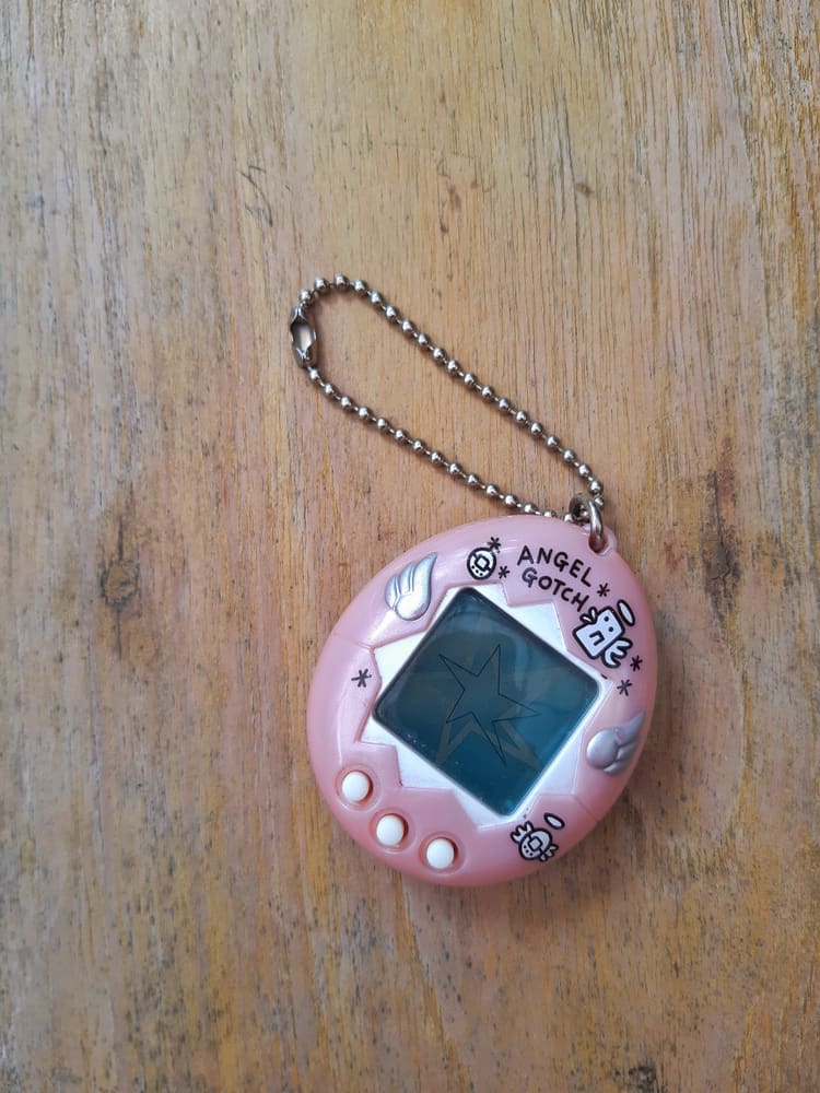 Tamagotchi pink Angel Gotch on wooden background.