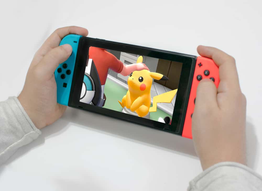 Young man playing pokémon let's go pikachu on a nintendo switch red and blue.