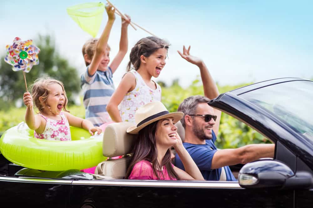 50 Best Road Trip Activities for Kids 1 A happy family riding on a convertible car on a road trip.