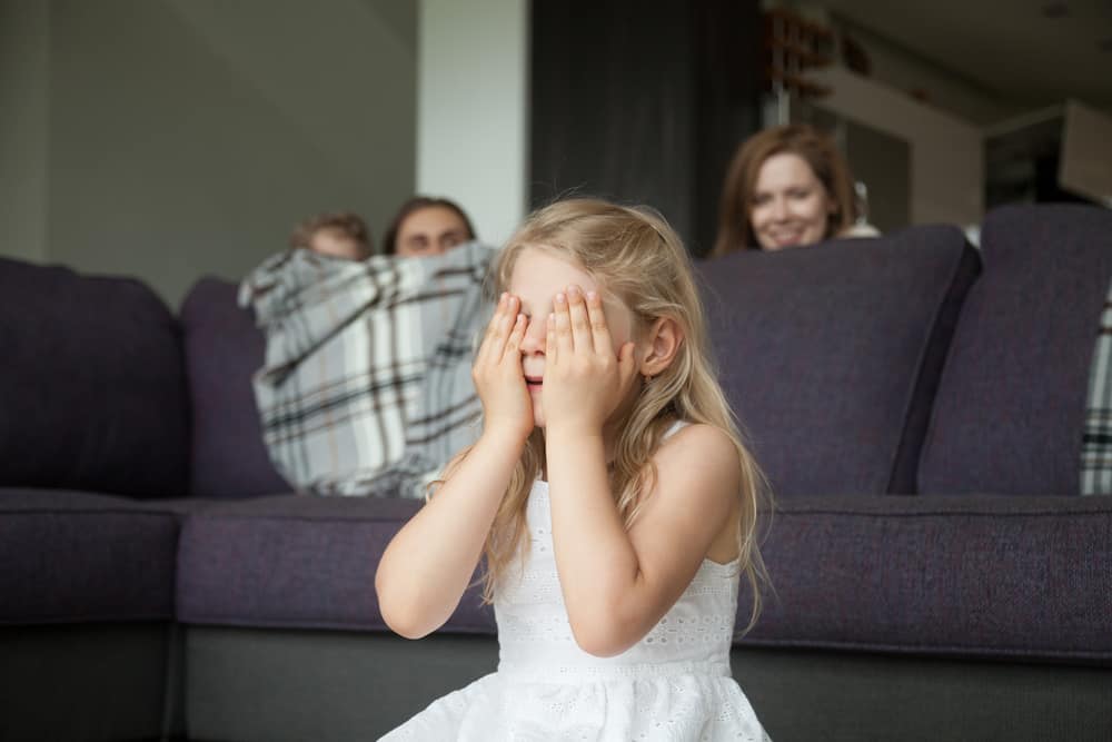 A family of four playing hide and seek together in the living room.