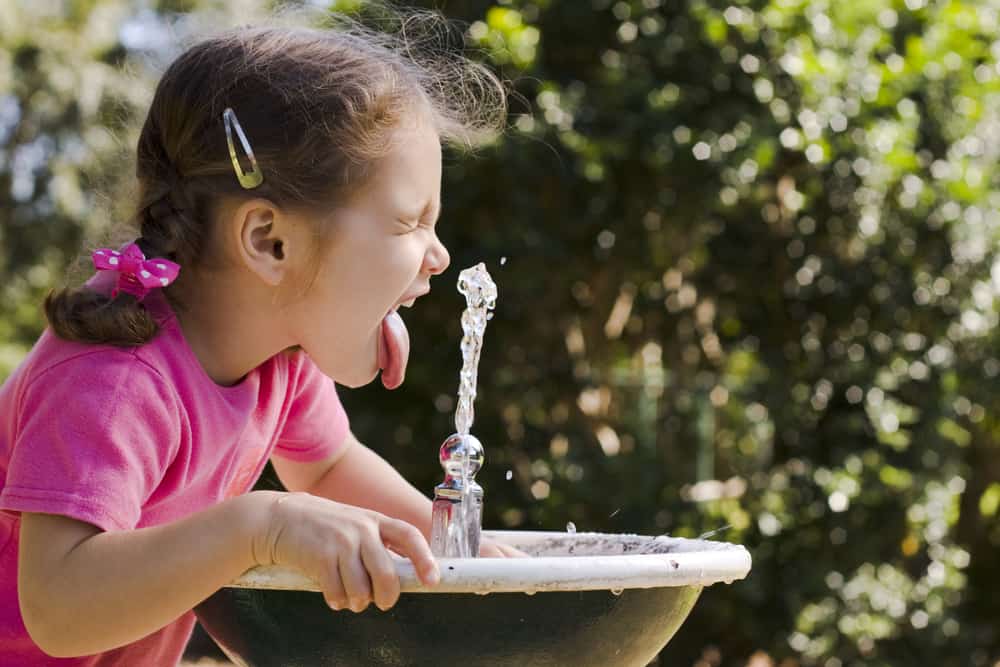 A girl drinking from a water fountain.