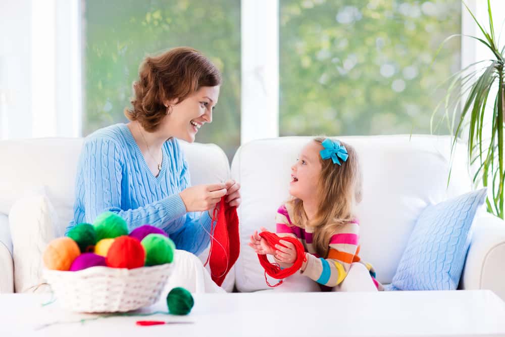 A mother and daughter knitting together in the living room.