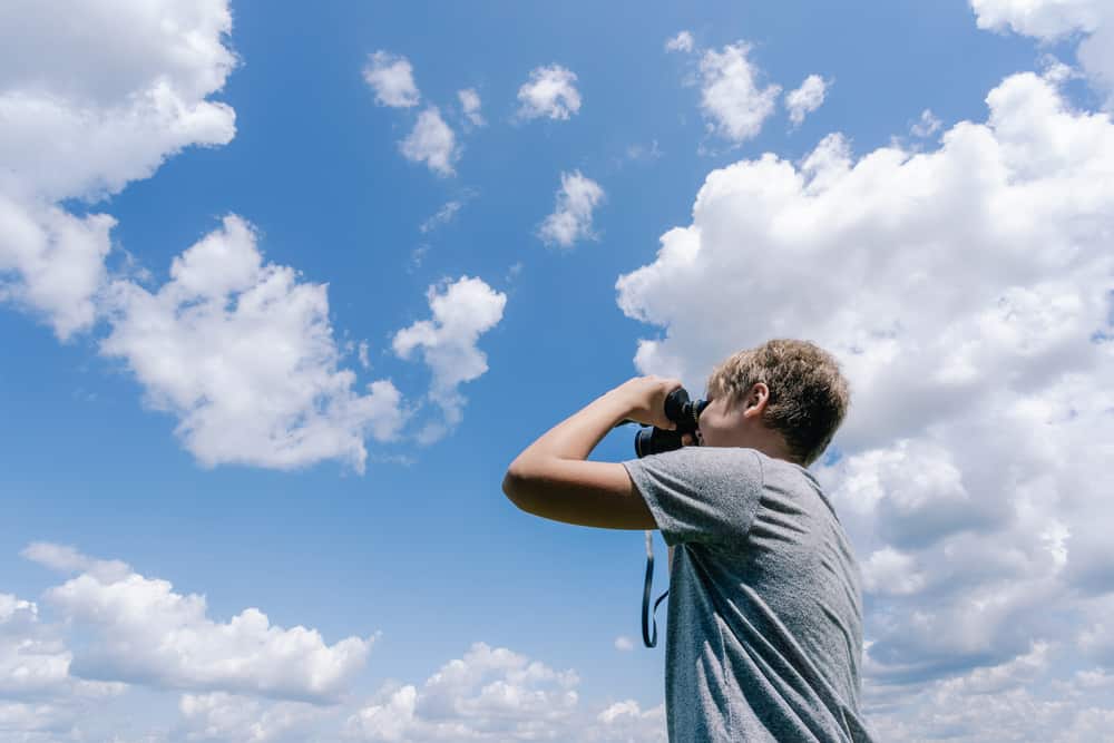 A boy taking pictures of clouds with his camera.