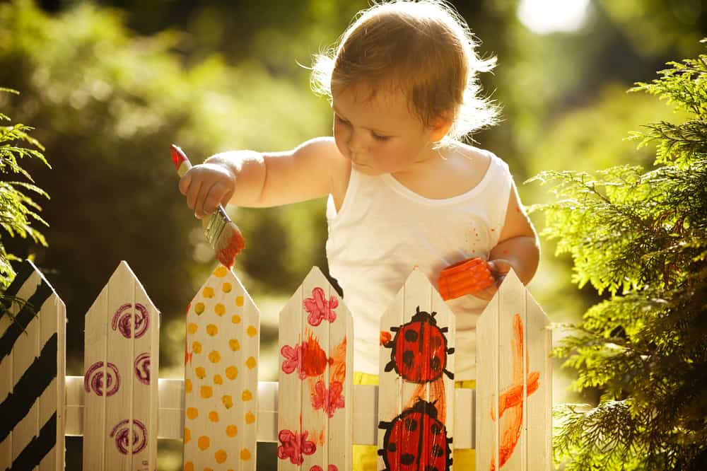 A toddler painting the fence.