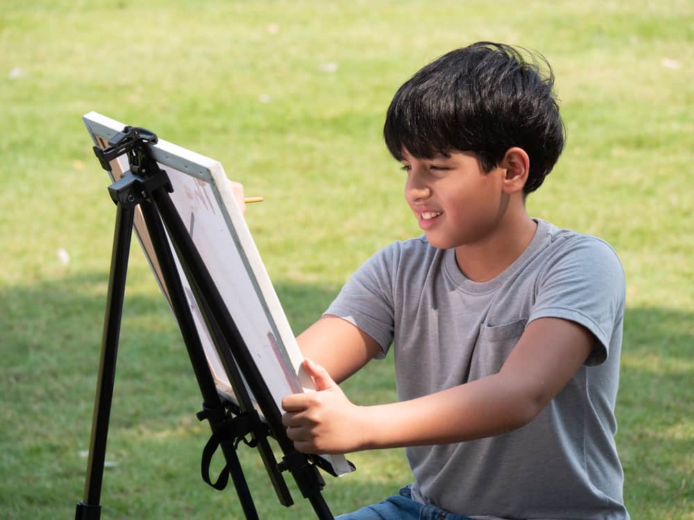 A boy painting on canvas in the backyard.