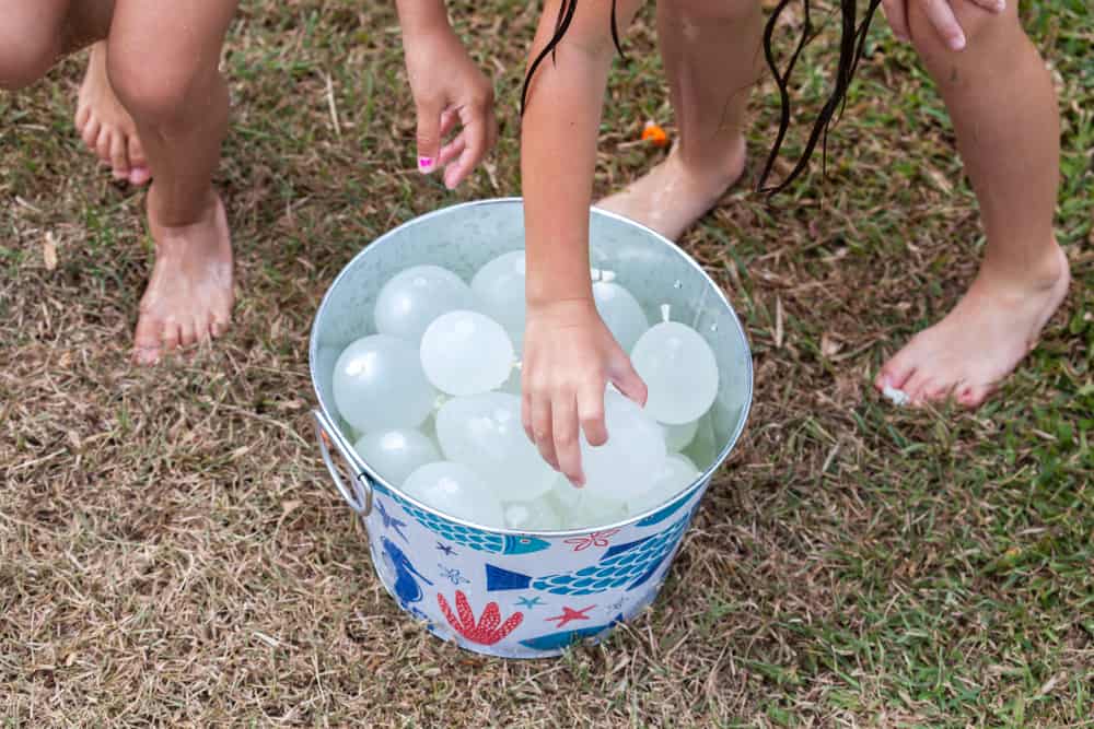 Kids playing with a bucket of water balloons.