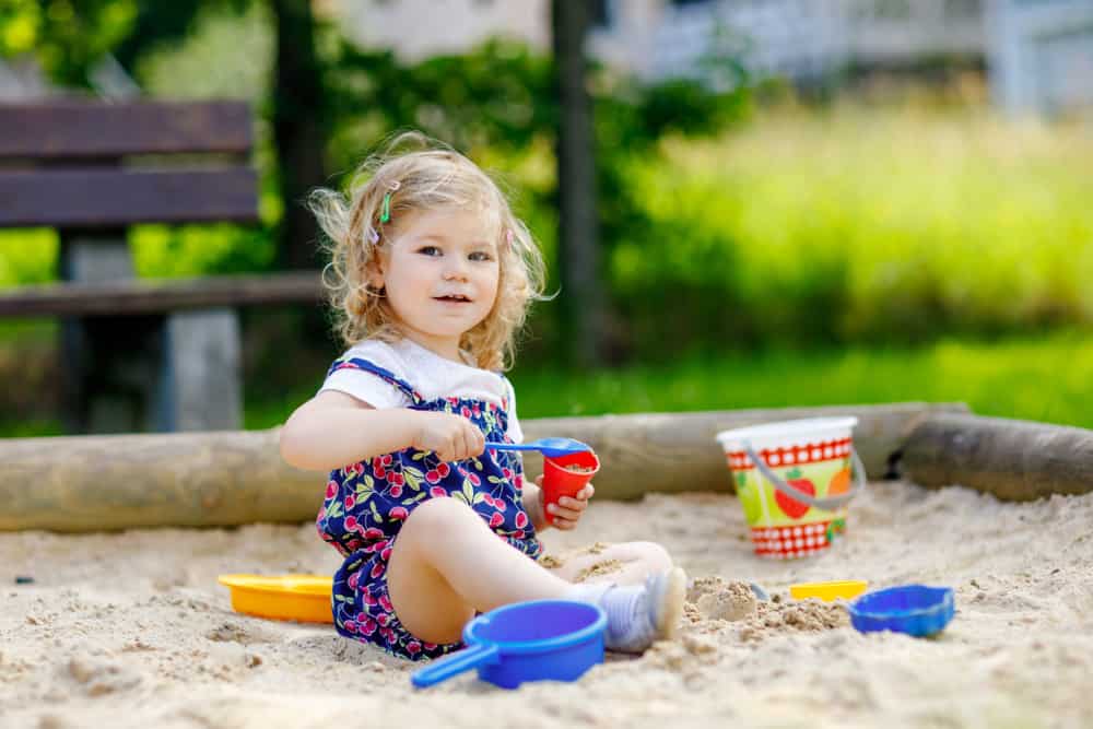 A toddle paying on the sand box with plastic toys.