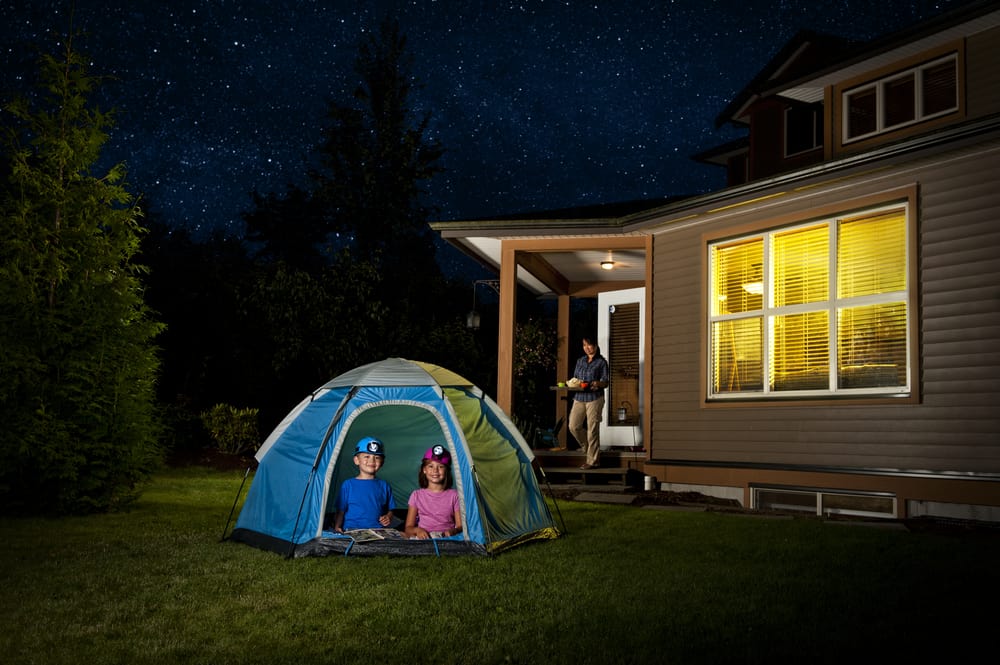 A couple of kids camping in a tent at the backyard.