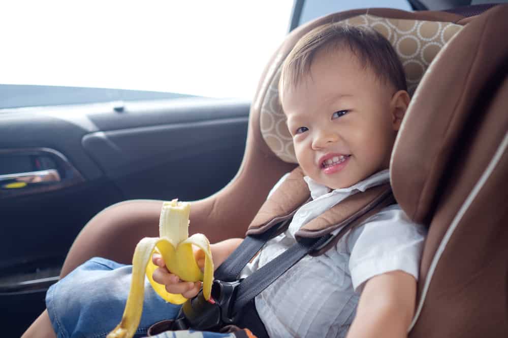 A toddler eating a banana inside the car.