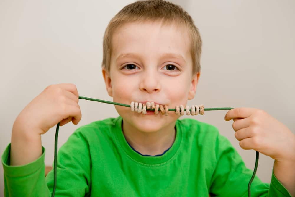 A boy playing with a cereal necklace.