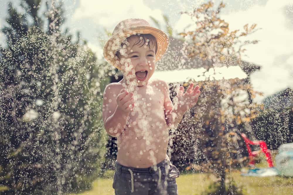 A boy playing with the sprinklers on a hot day.