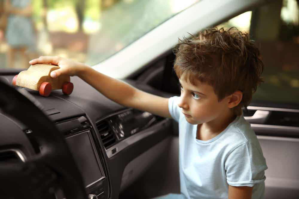 A kid playing with a wooden toy car at the passenger seat.