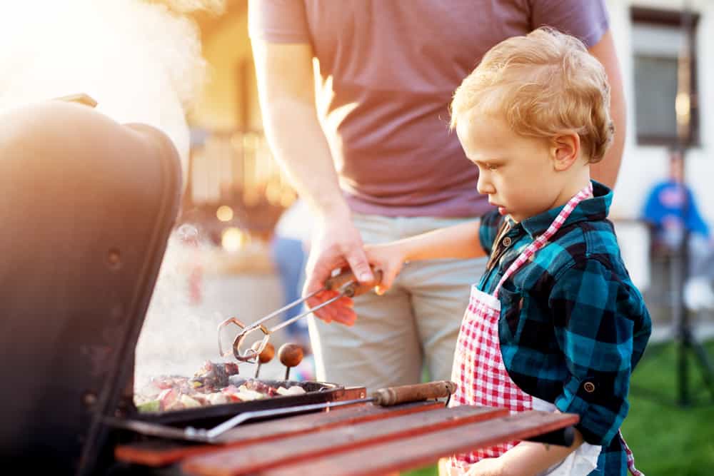 A toddler cooking on the grill with a parent.