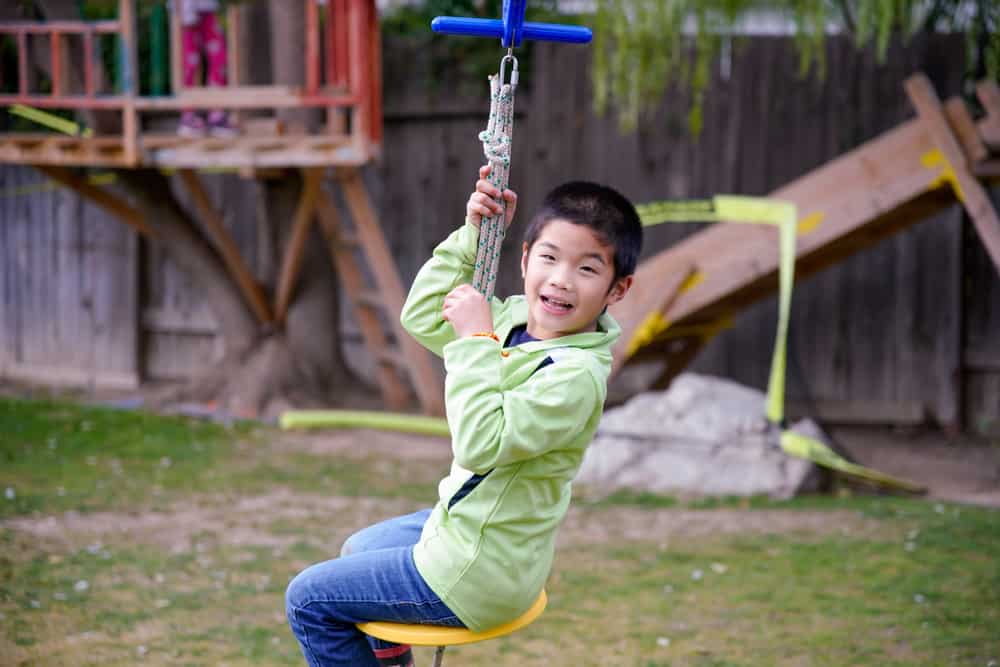 A boy playing on the zip line in the backyard.