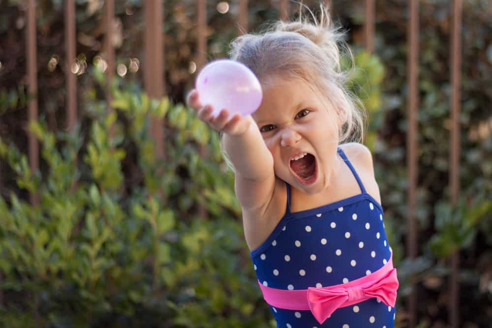 A girl playing with a water balloon in the backyard.