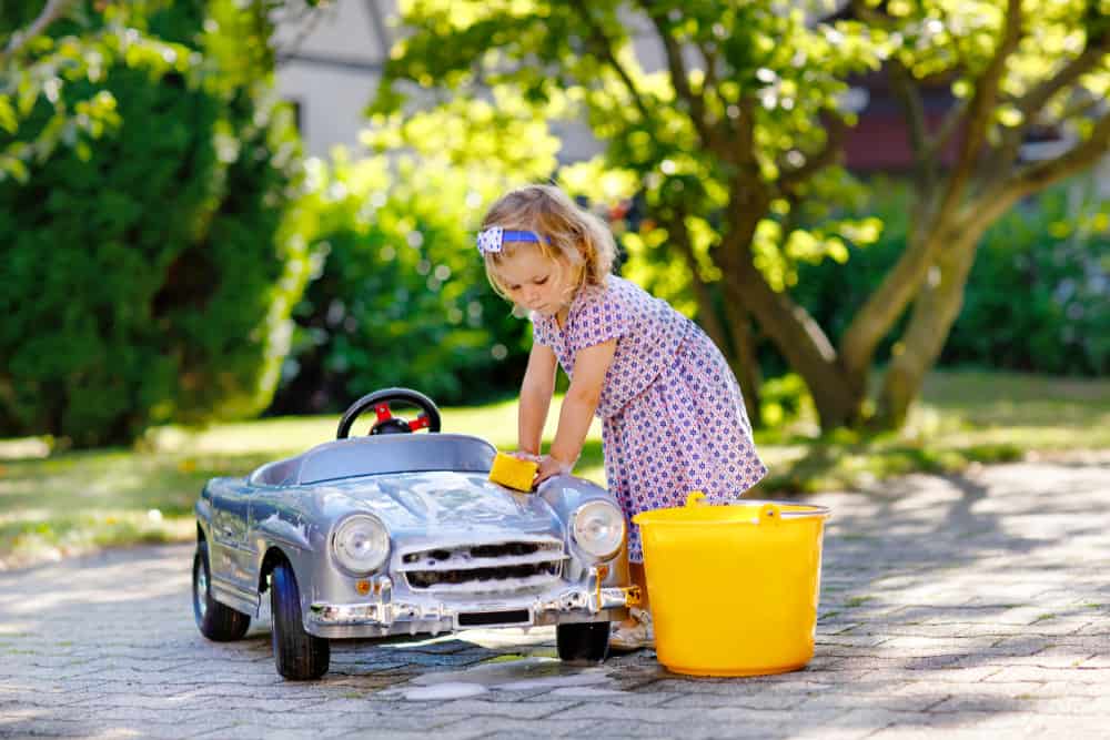 A girl cleaning her toy car in the backyard.