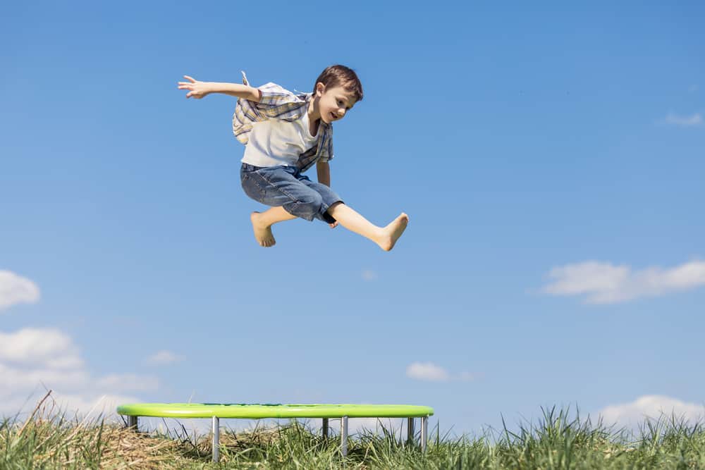 A boy playing on the trampoline on the grass lawn.