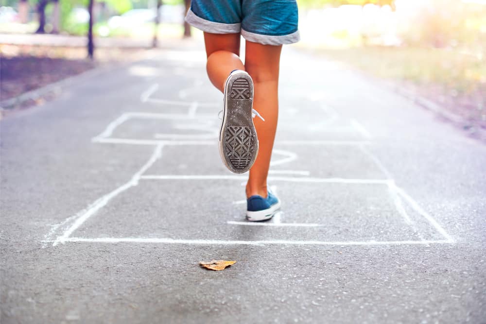 Girl playing hop scotch on the sidewalk.