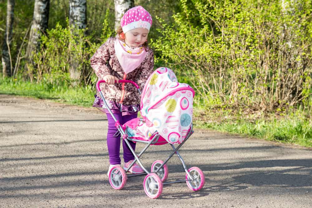 A girl playing with her baby doll on a stroller.