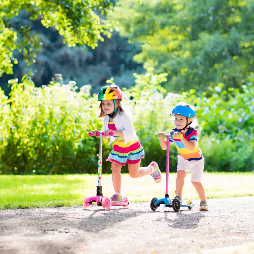 Two girls riding on scooters at the park.