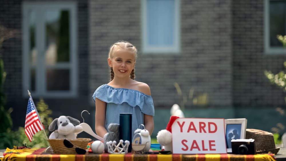 A girl selling items at a yard sale.