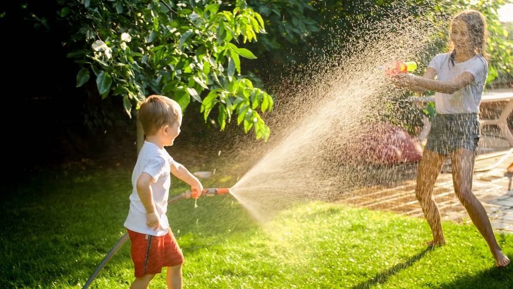 Siblings having a water fight in the backyard.