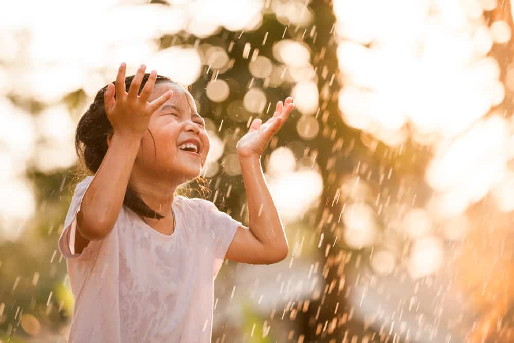 A girl is playing under the rain.