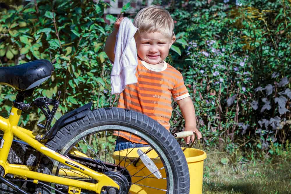 A kid trying to wash a bike bigger than him.