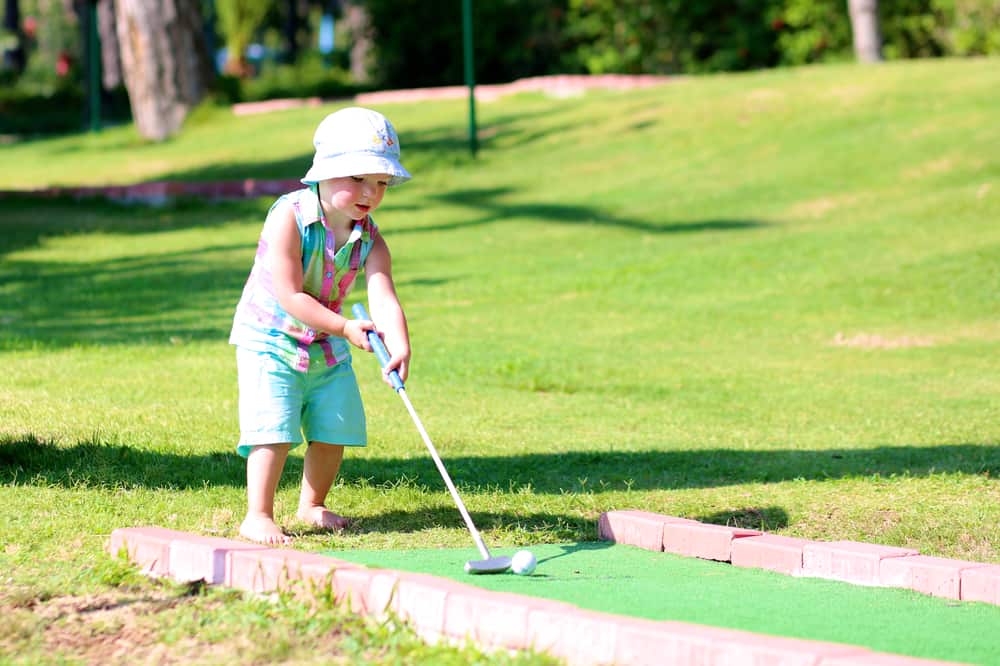 A toddler playing miniature golf.