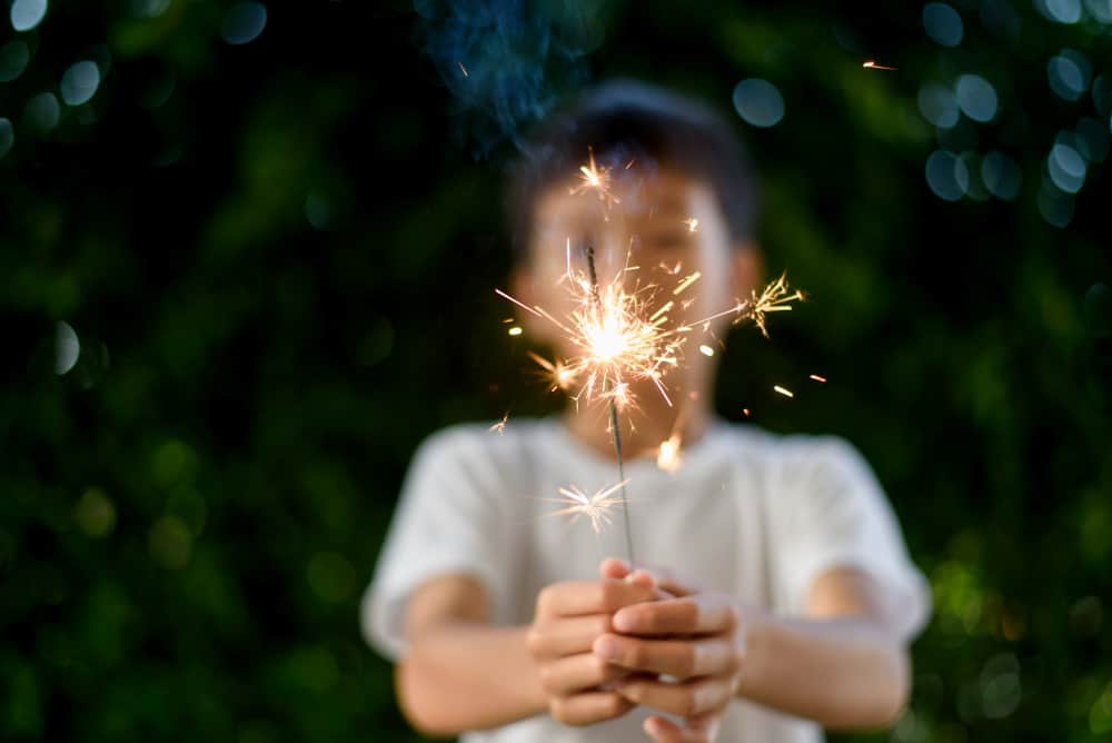 A boy playing with sparklers at the backyard.