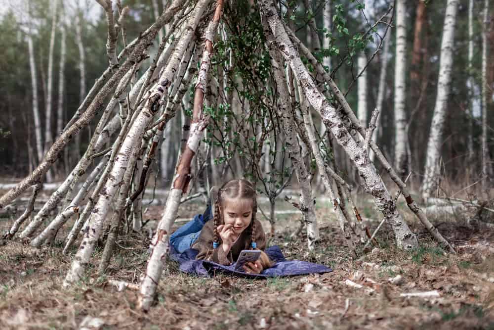 A girl in a makeshift stick house teepee.