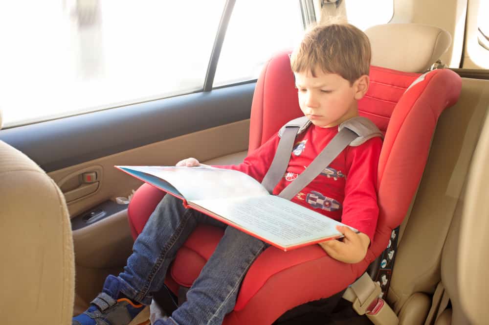 A kid reading a book inside the car.