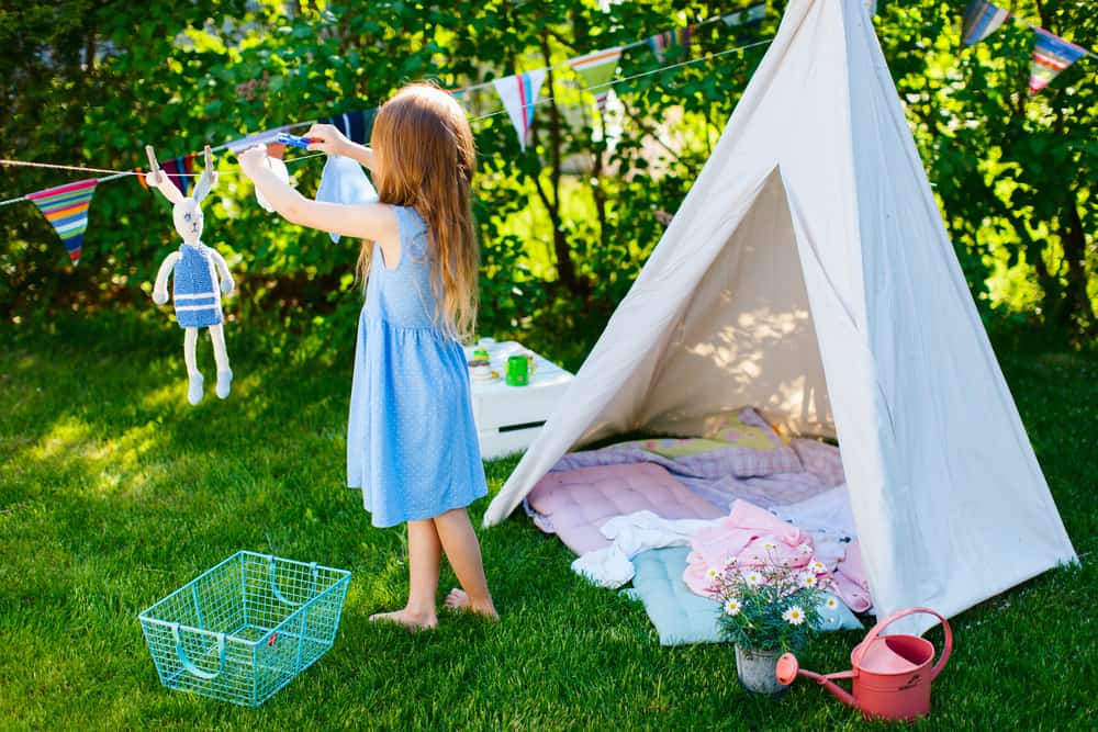 A girl playing with her teepee in the backyard.