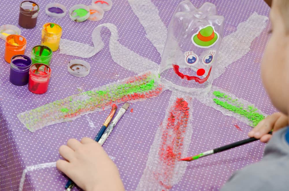 A boy is painting on the empty plastic bottle.