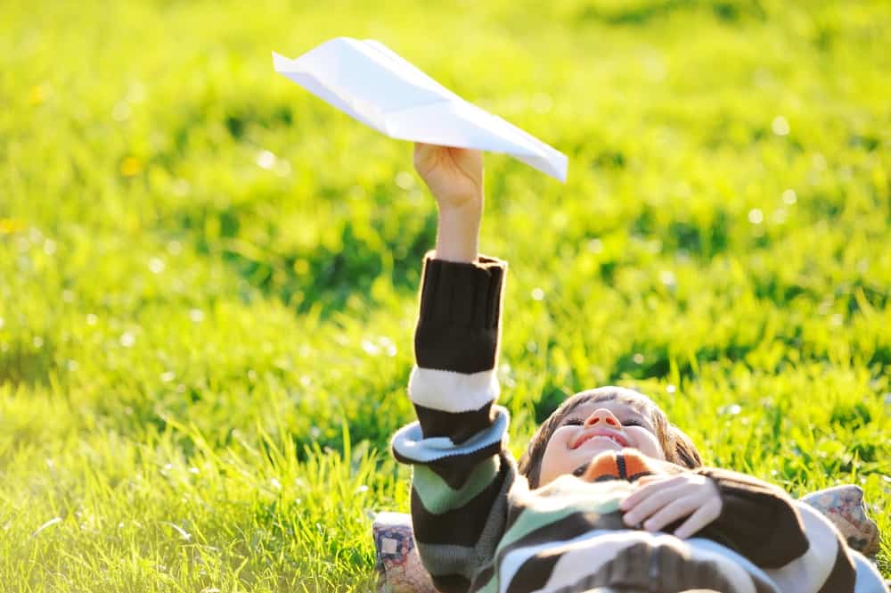 A boy playing with a paper airplane.