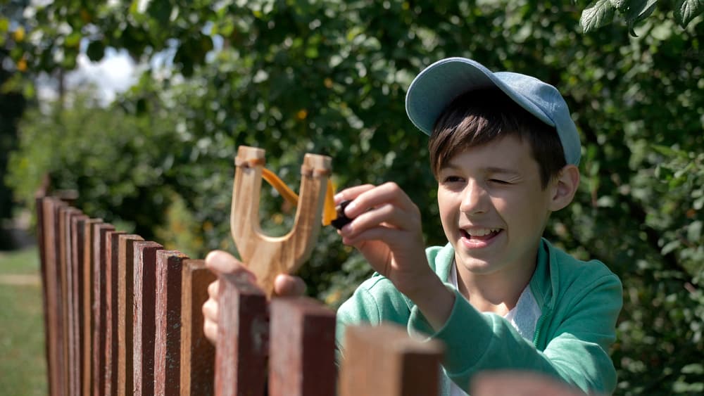 A boy playing with a wooden slingshot.