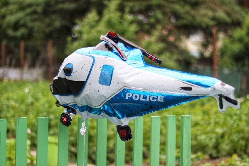 Balloon helicopter over a green picket fence.