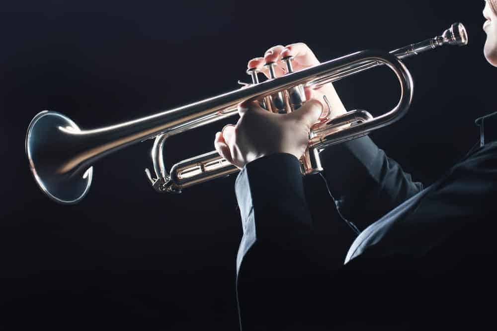 9 Popular Types of Trumpets Explained 4 Musician playing a trumpet against black background.