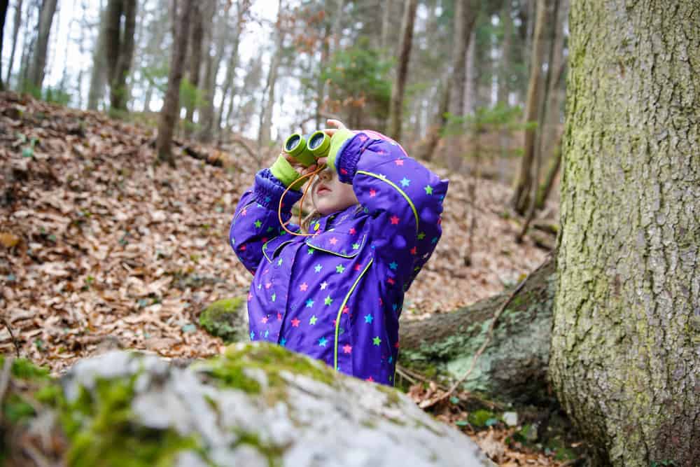 Girl looking through the binoculars in the forest.
