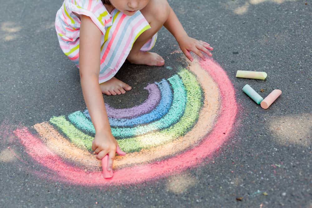 Girl drawing a rainbow using colored chalks on the asphalt.