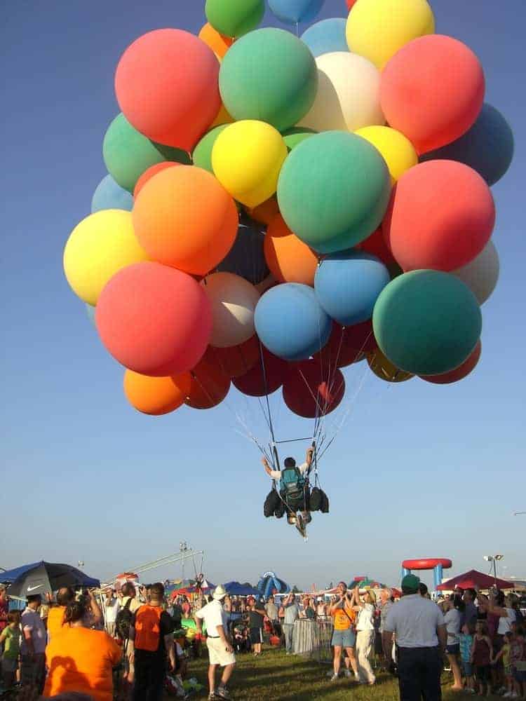 A man flies away in a cluster balloon.