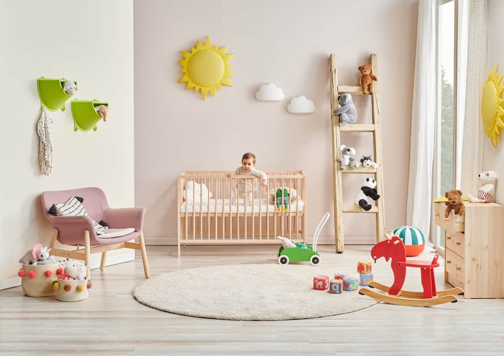 Nursery room with a cot bed, a wooden ladder, pink armchair, and a rocking horse.