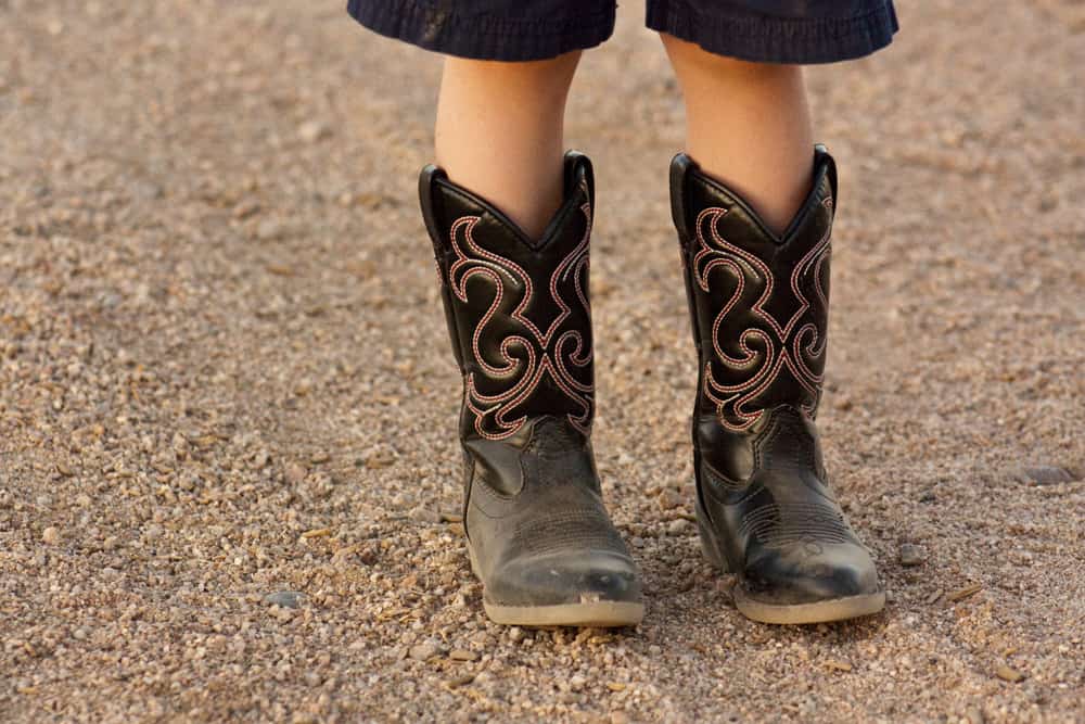 Kid wearing cowboy boots standing on the gravel.