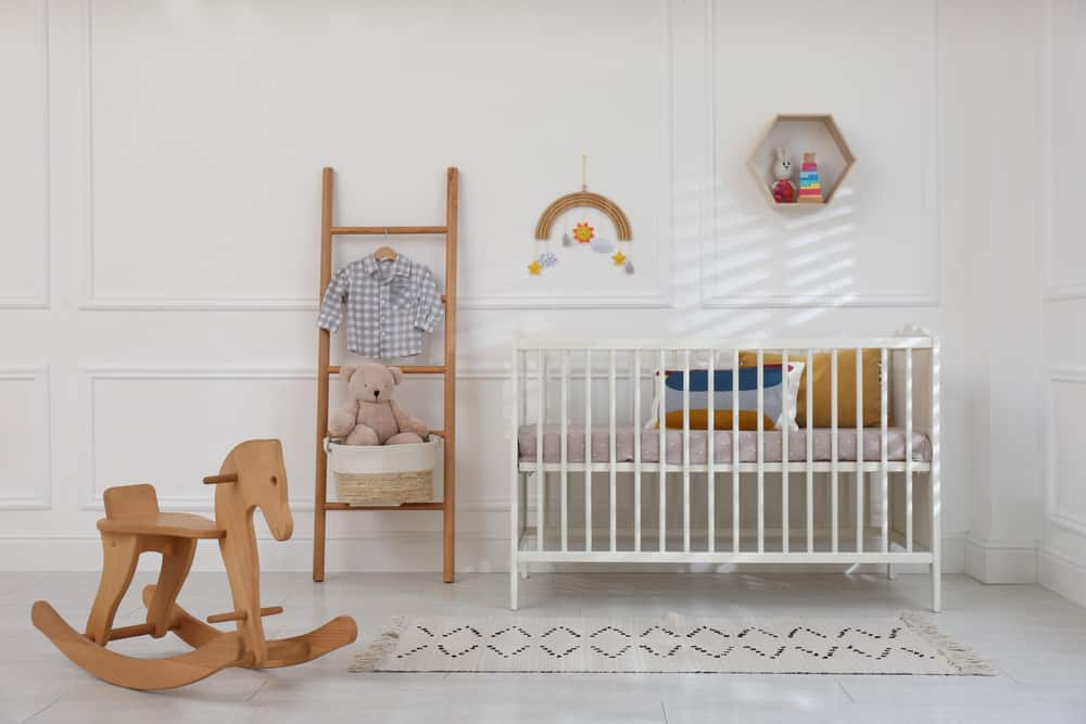 Nursery room with a wooden ladder, a rocking horse, and a white crib complemented with a tasseled runner.